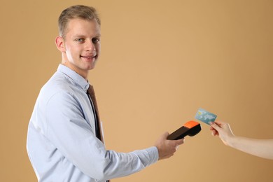 Happy young man taking payment from client via terminal on beige background