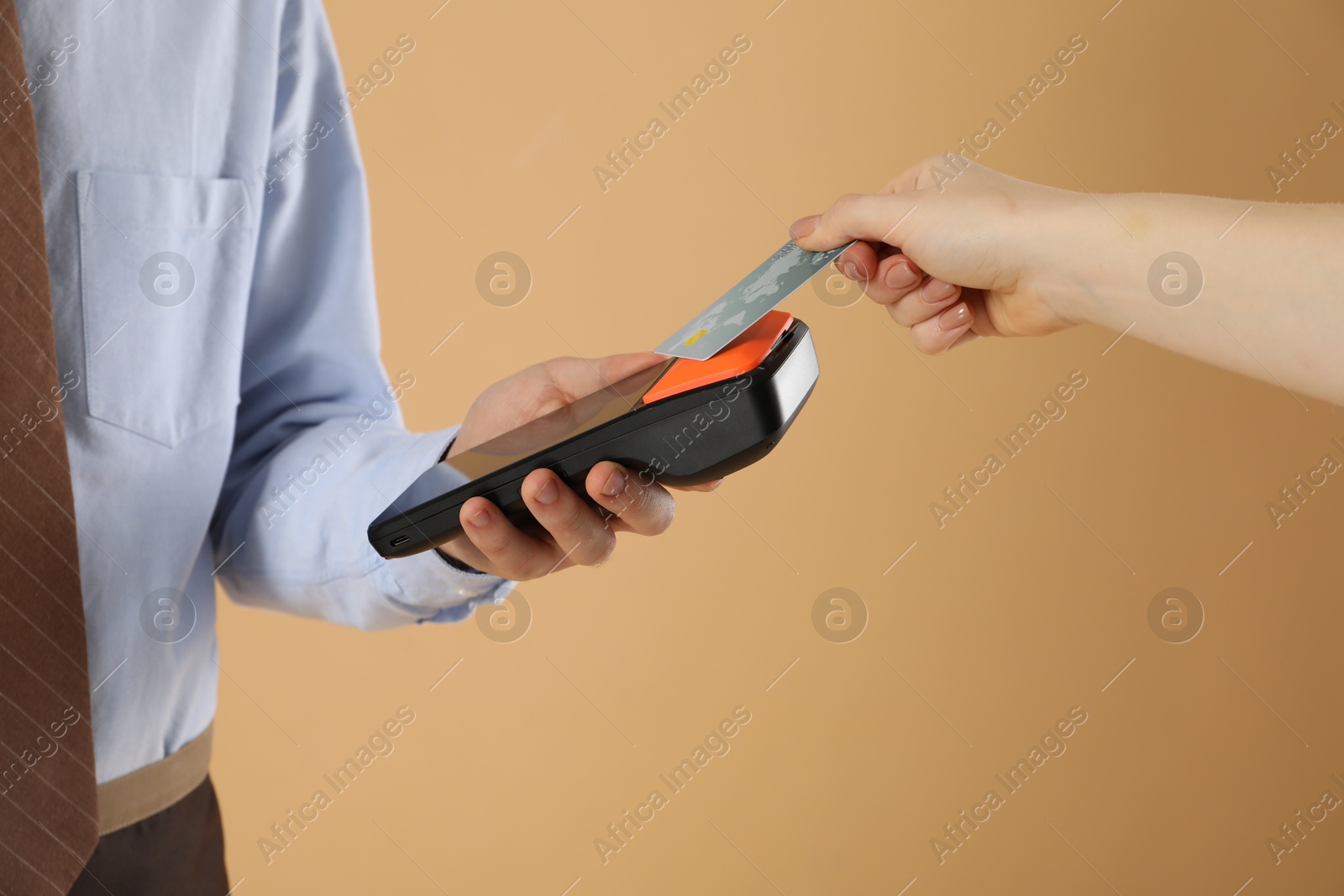 Photo of Young man taking payment from client via terminal on beige background, closeup