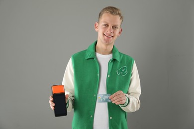 Photo of Happy young man with payment terminal and debit card on light grey background