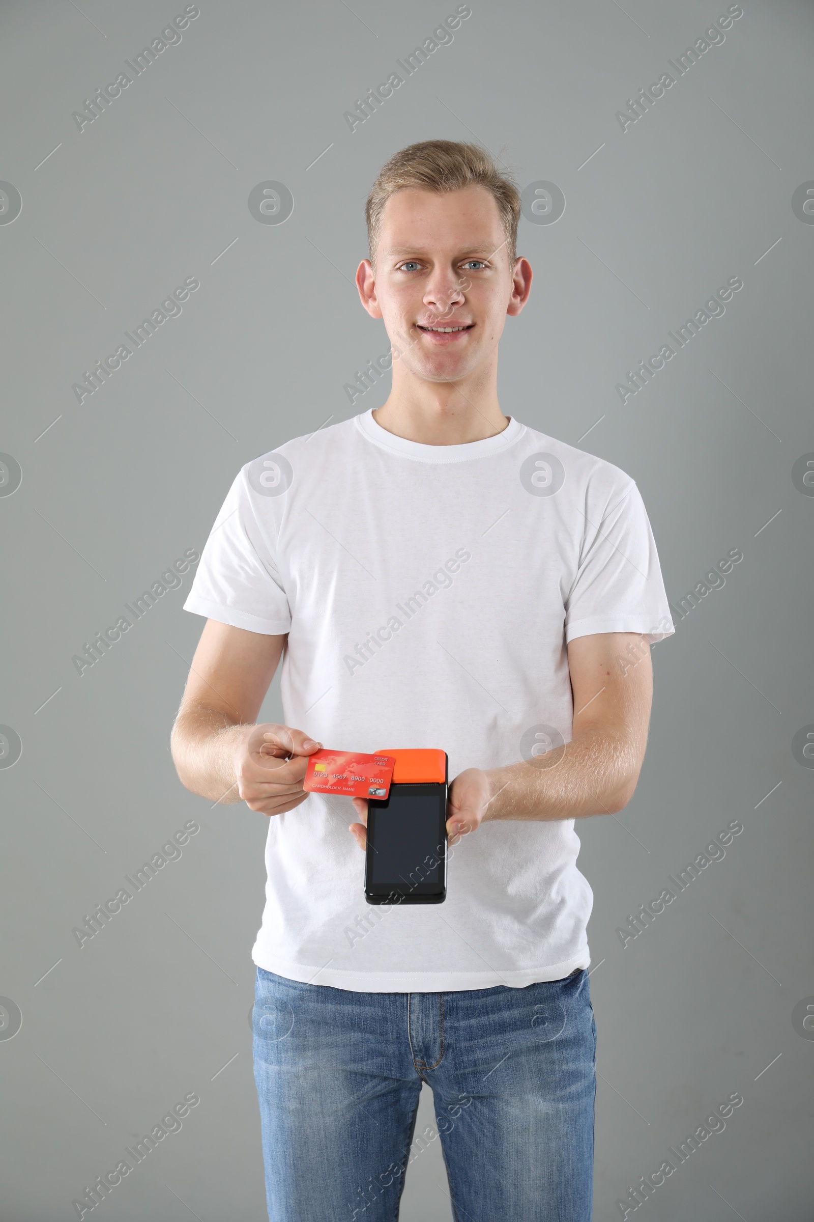 Photo of Happy young man with payment terminal and debit card on light grey background