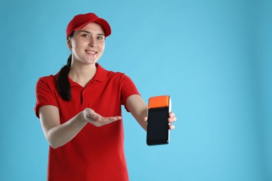 Photo of Happy courier with payment terminal on light blue background, space for text