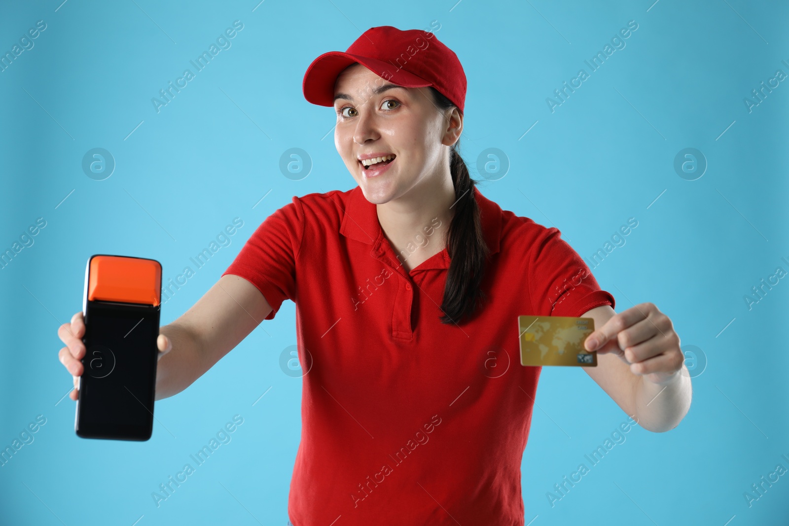 Photo of Happy courier with payment terminal and credit card on light blue background