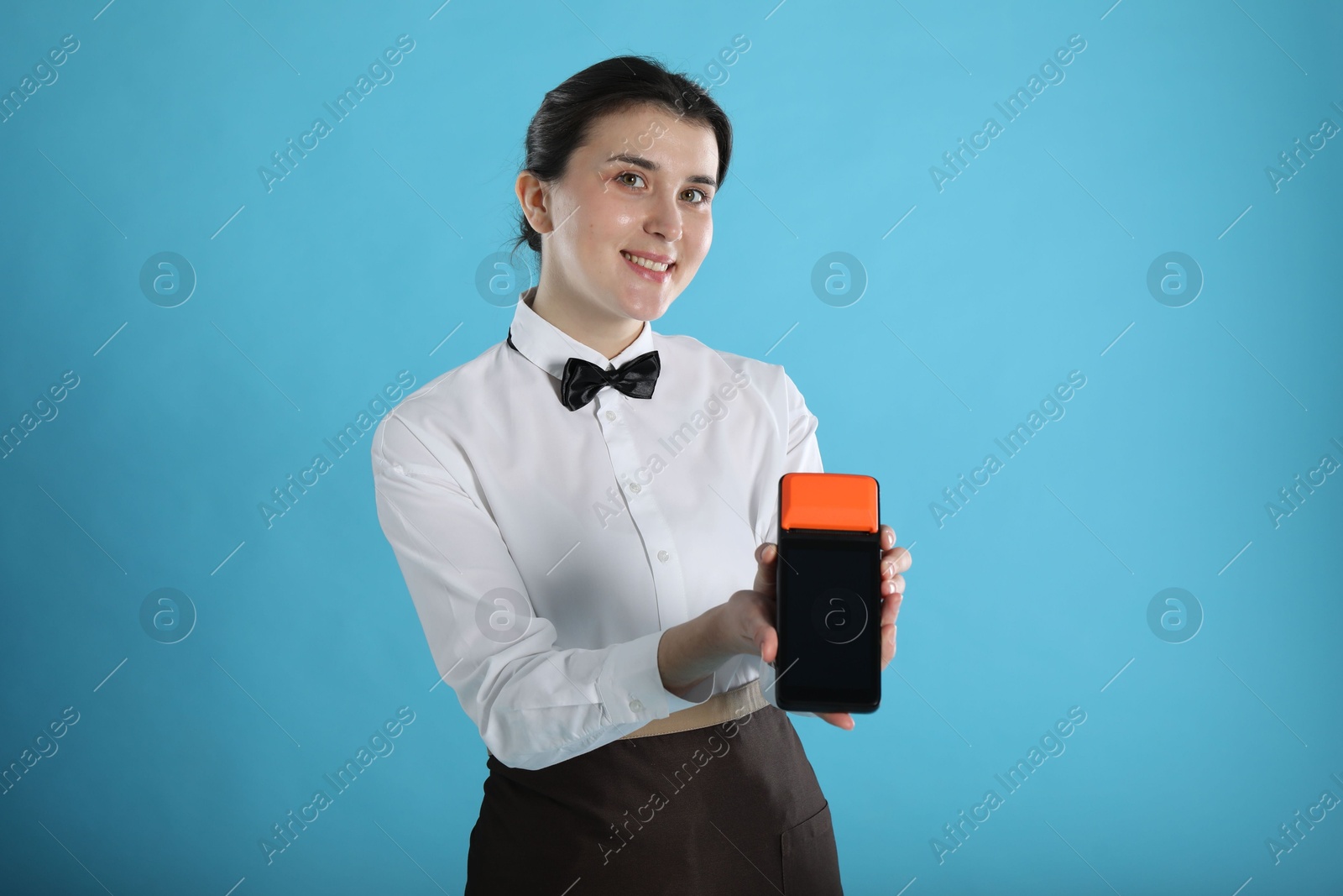 Photo of Happy waitress with payment terminal on light blue background