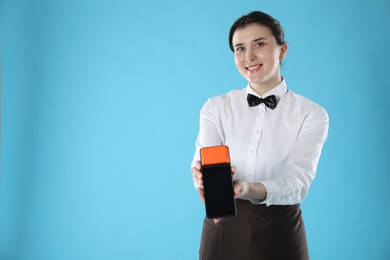 Photo of Happy waitress with payment terminal on light blue background, space for text