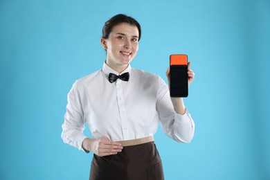 Photo of Happy waitress with payment terminal on light blue background