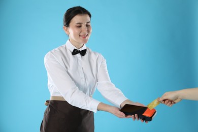 Photo of Waitress taking payment from client via terminal on light blue background