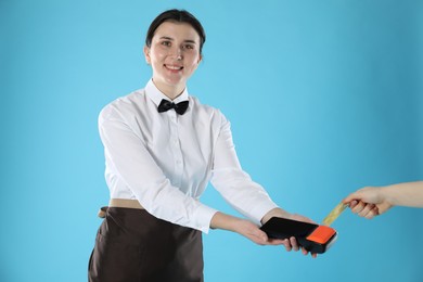 Photo of Waitress taking payment from client via terminal on light blue background