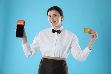 Photo of Happy waitress with payment terminal and credit card on light blue background