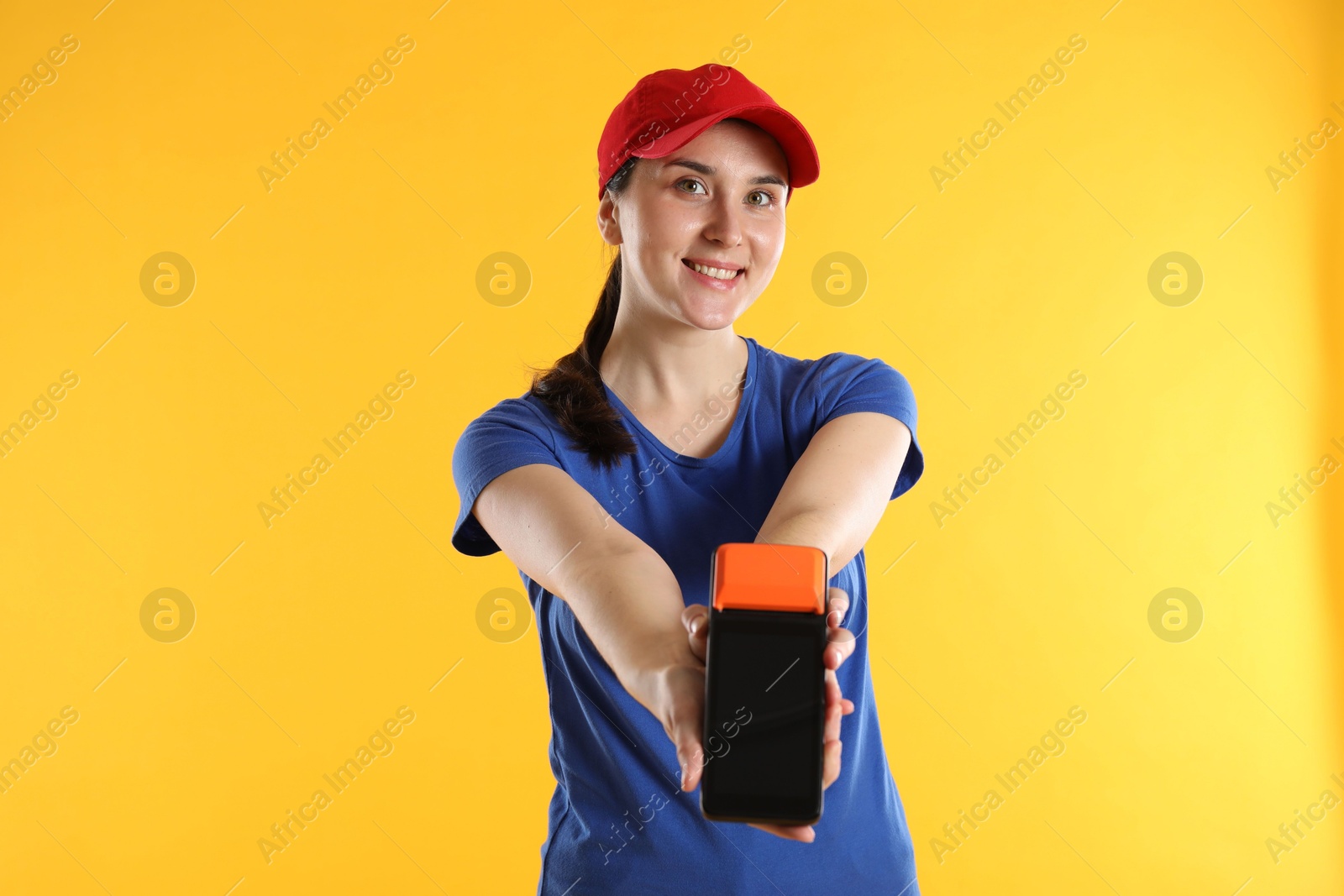 Photo of Happy courier with payment terminal on yellow background