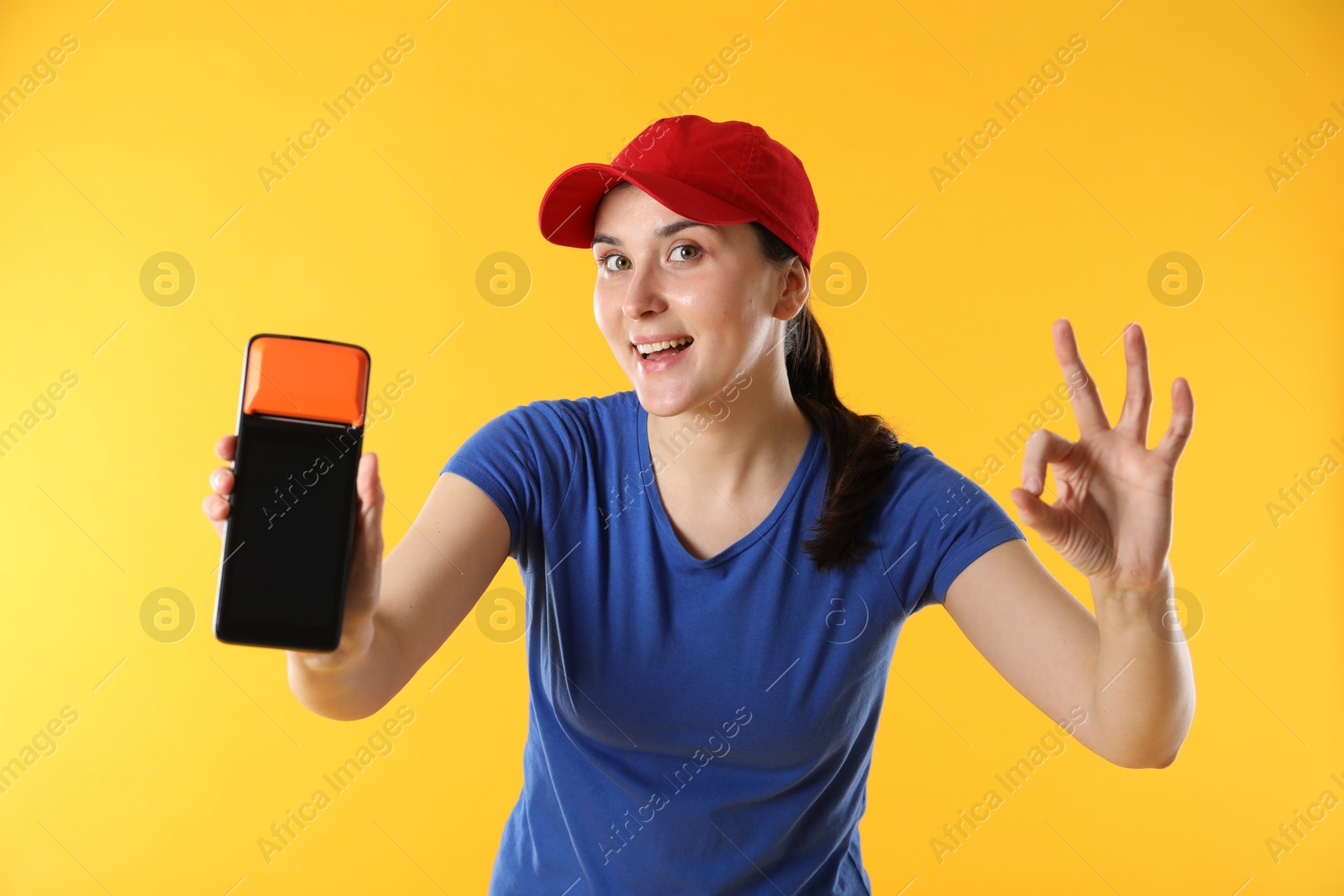 Photo of Happy courier with payment terminal showing OK gesture on yellow background