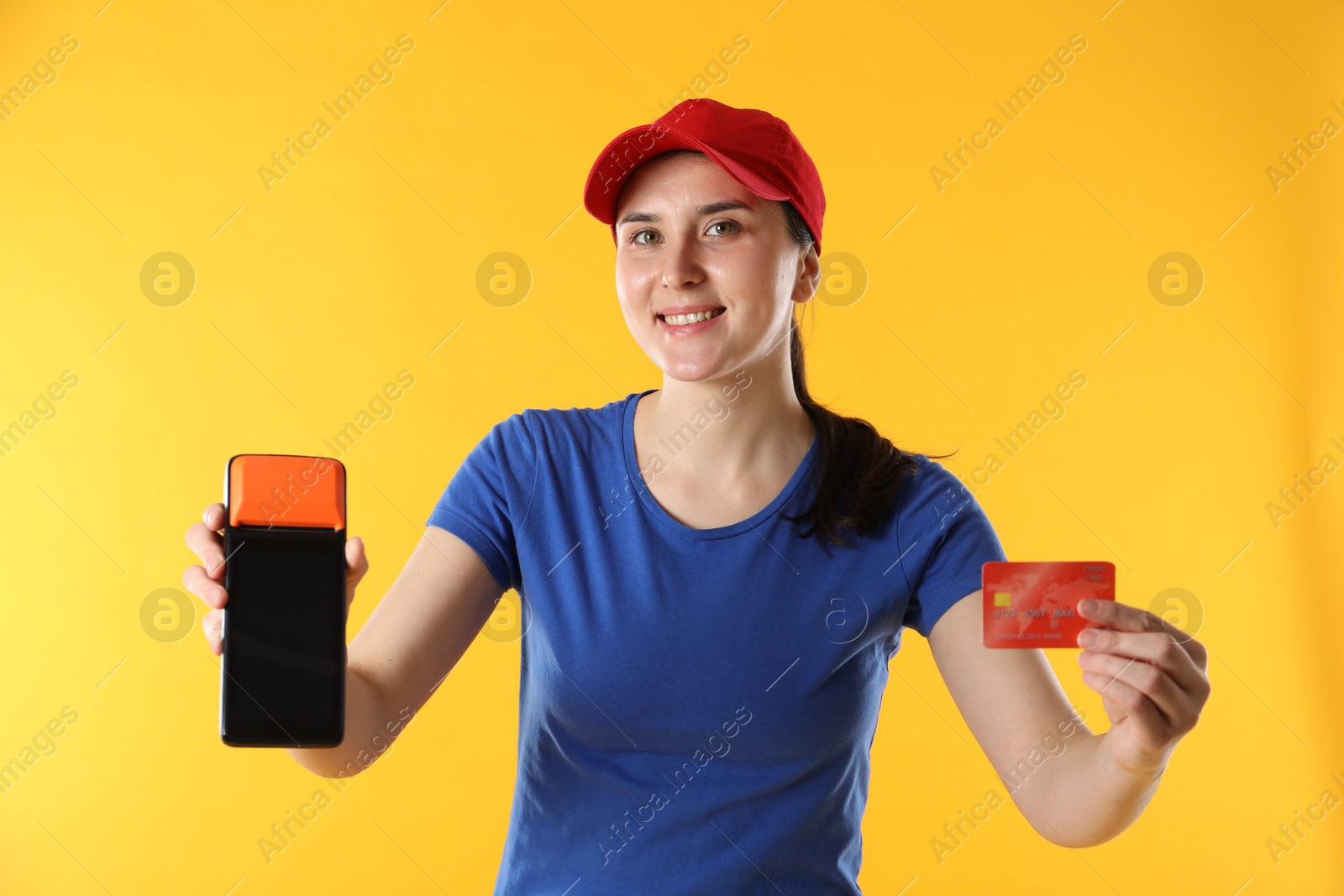 Photo of Happy courier with payment terminal and credit card on yellow background