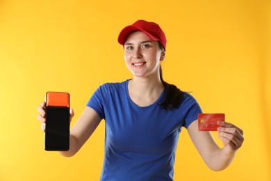 Photo of Happy courier with payment terminal and credit card on yellow background