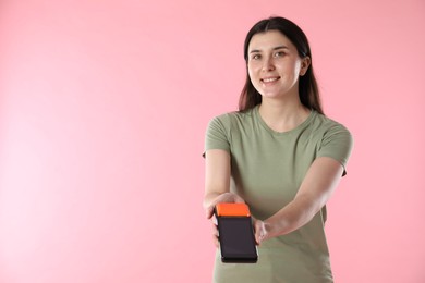 Happy young woman with payment terminal on pink background, space for text