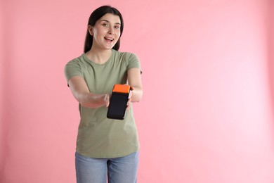 Happy young woman with payment terminal on pink background, space for text