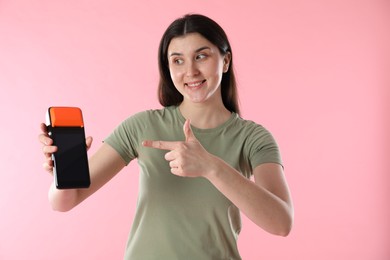 Photo of Happy young woman with payment terminal on pink background