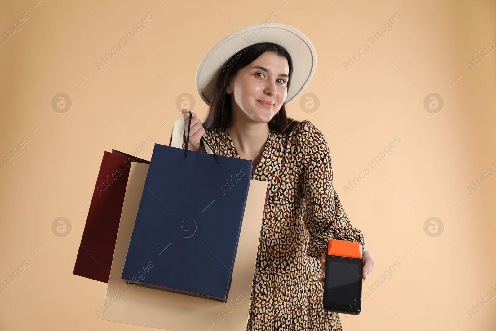 Photo of Young woman with payment terminal and shopping bags on beige background