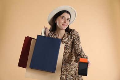 Young woman with payment terminal and shopping bags on beige background