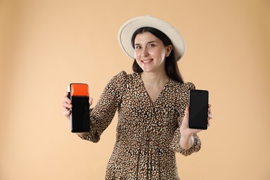 Happy young woman with payment terminal and smartphone on beige background