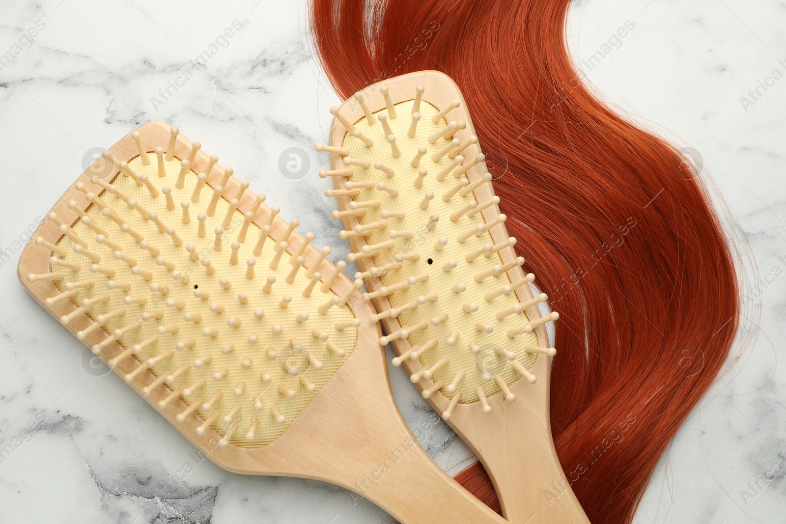 Photo of Wooden brushes and lock of hair on white marble table, flat lay