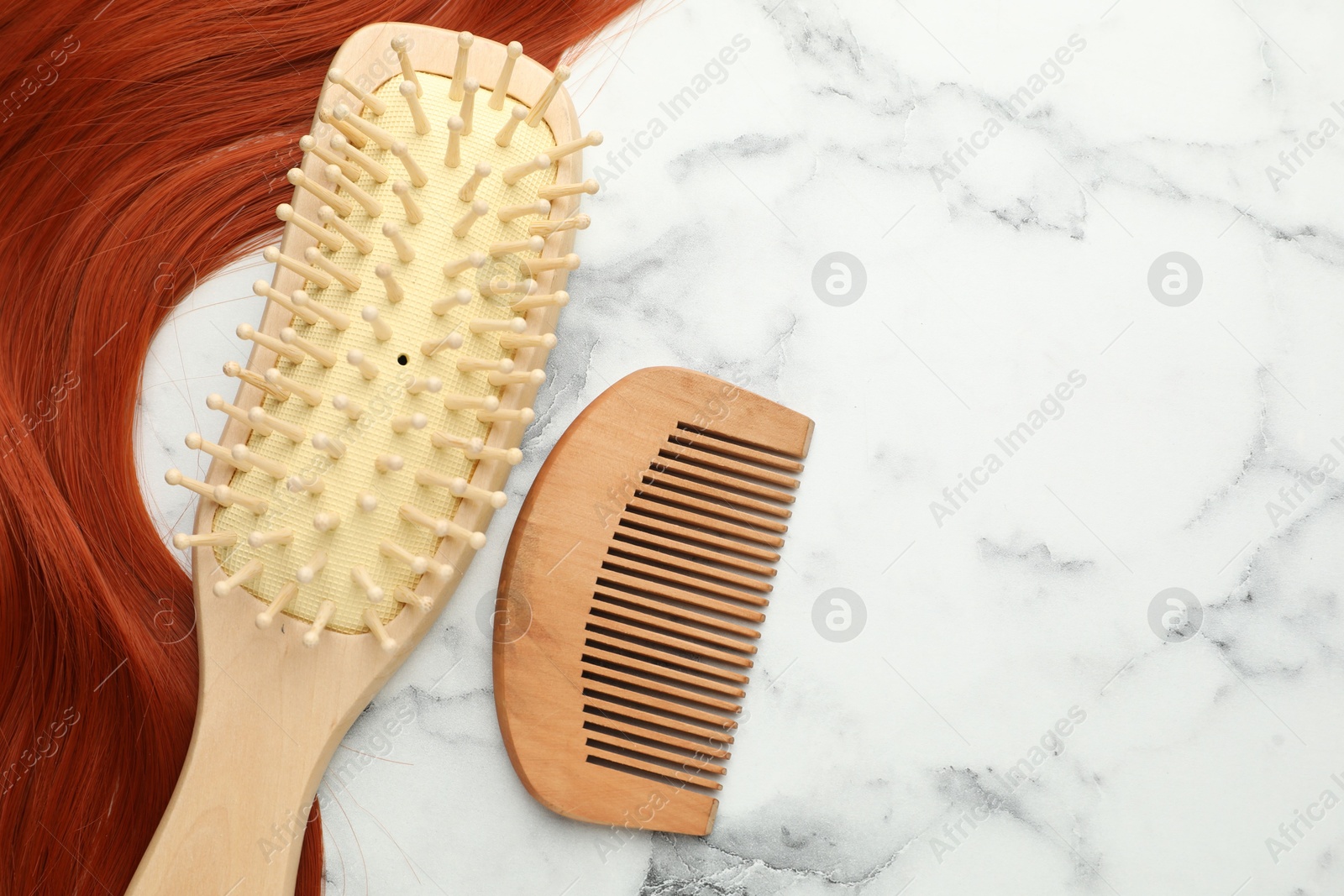 Photo of Wooden brush, comb and lock of hair on white marble table, flat lay. Space for text