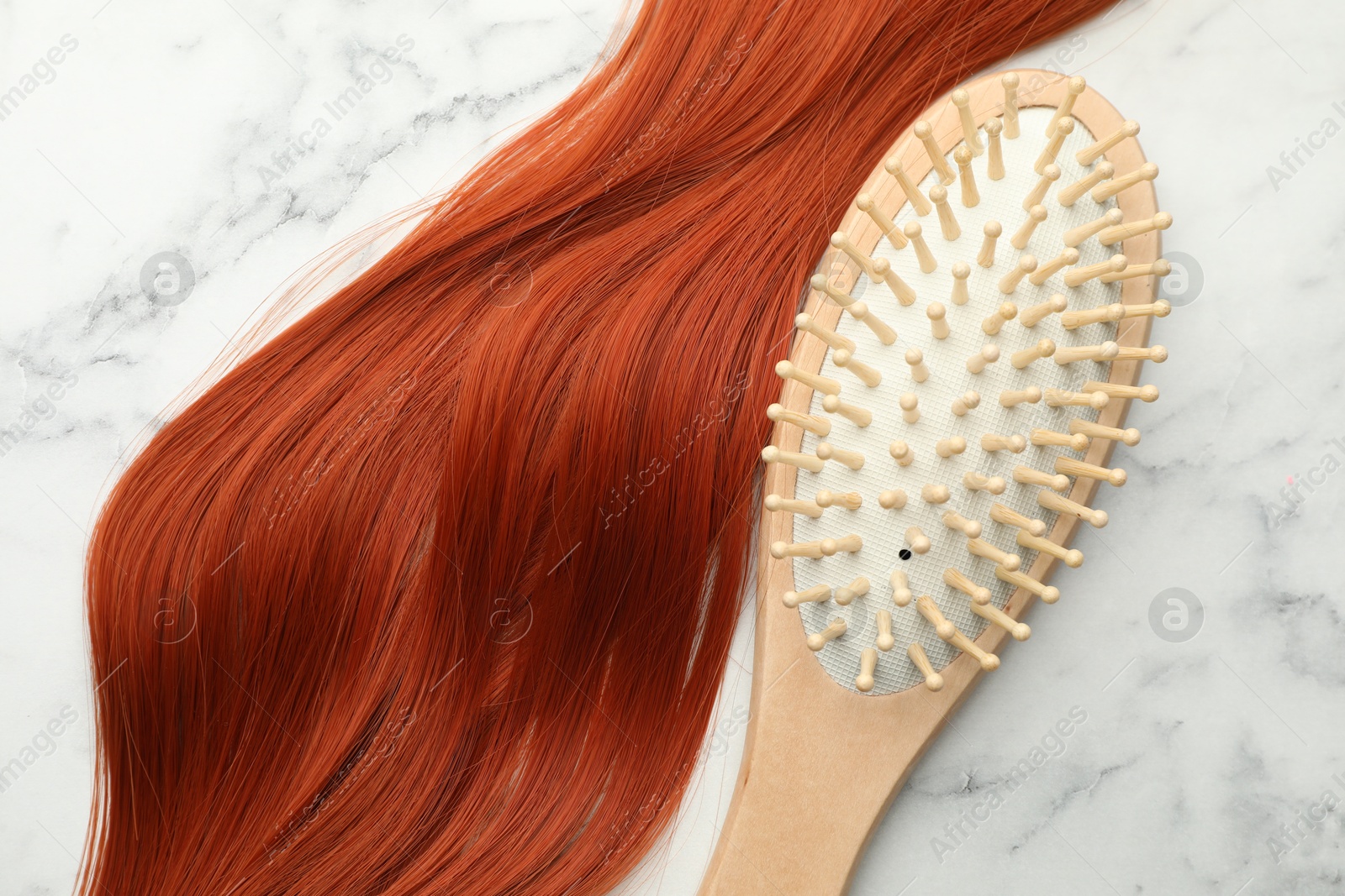 Photo of Wooden brush and lock of hair on white marble table, top view