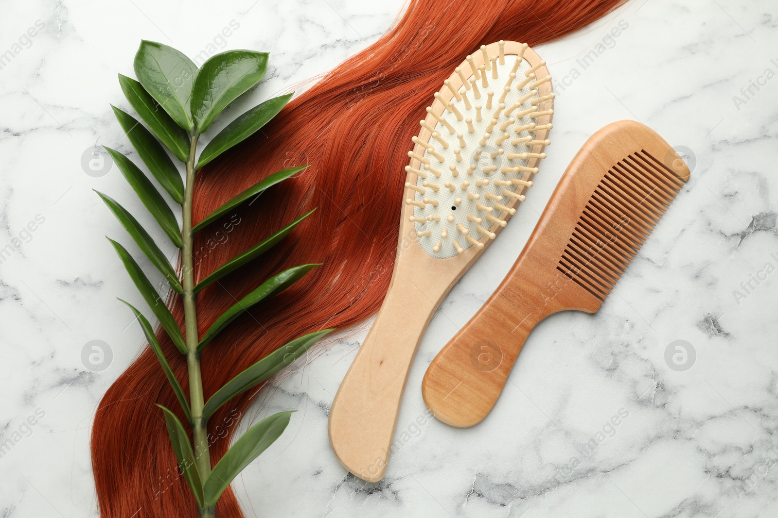 Photo of Wooden brush, comb, branch with leaves and lock of hair on white marble table, flat lay