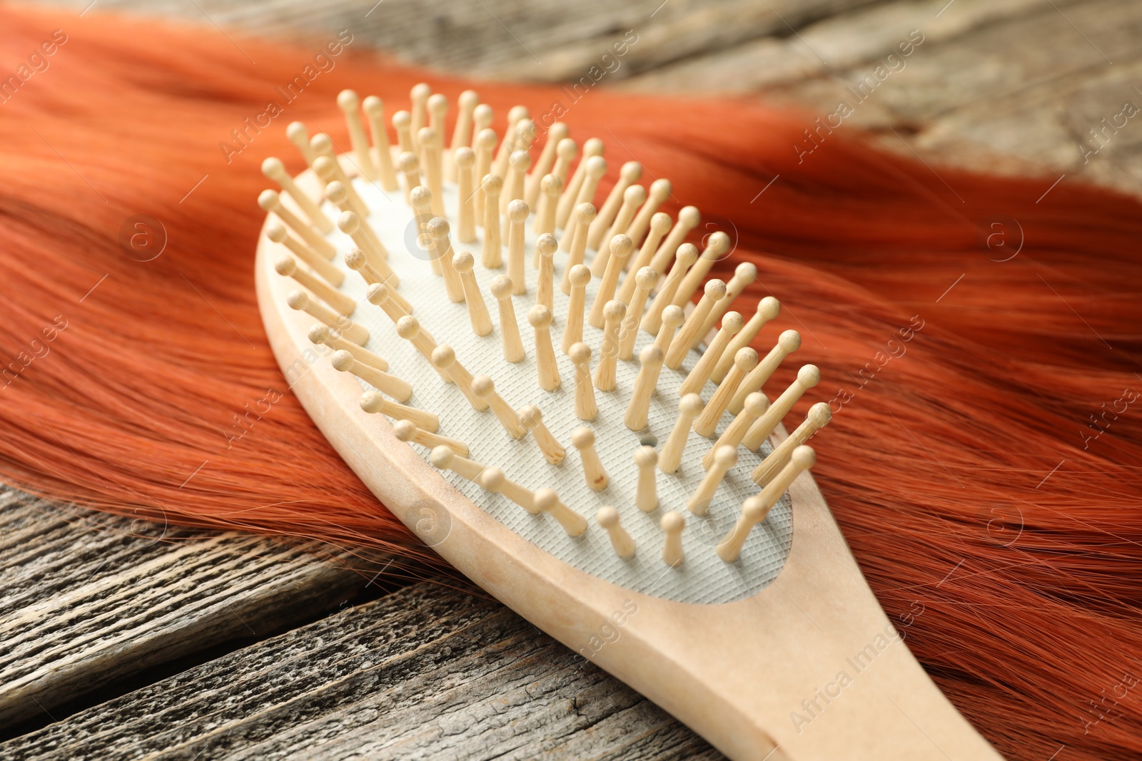 Photo of Brush and lock of hair on wooden table, closeup