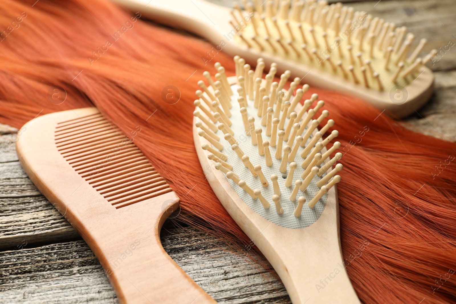 Photo of Different brushes, comb and lock of hair on wooden table, closeup