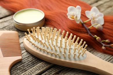 Photo of Brush, comb, wax, orchid branch and lock of hair on wooden table, closeup