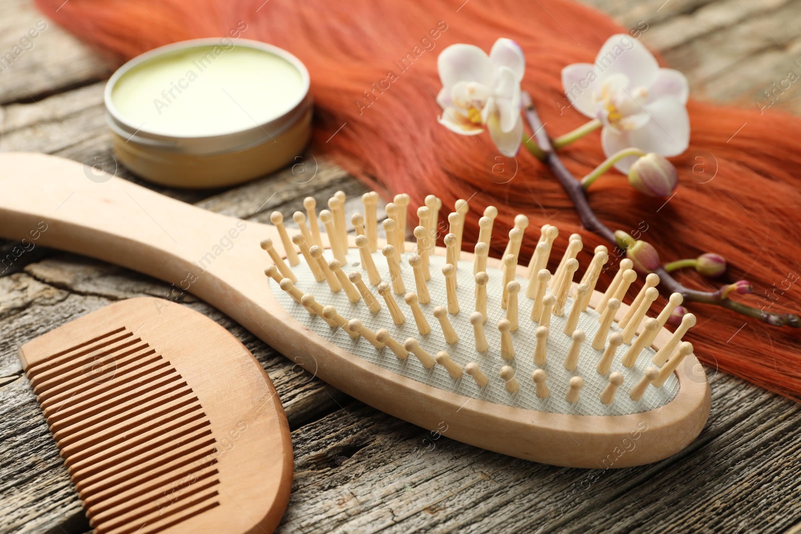 Photo of Brush, comb, wax, orchid branch and lock of hair on wooden table, closeup