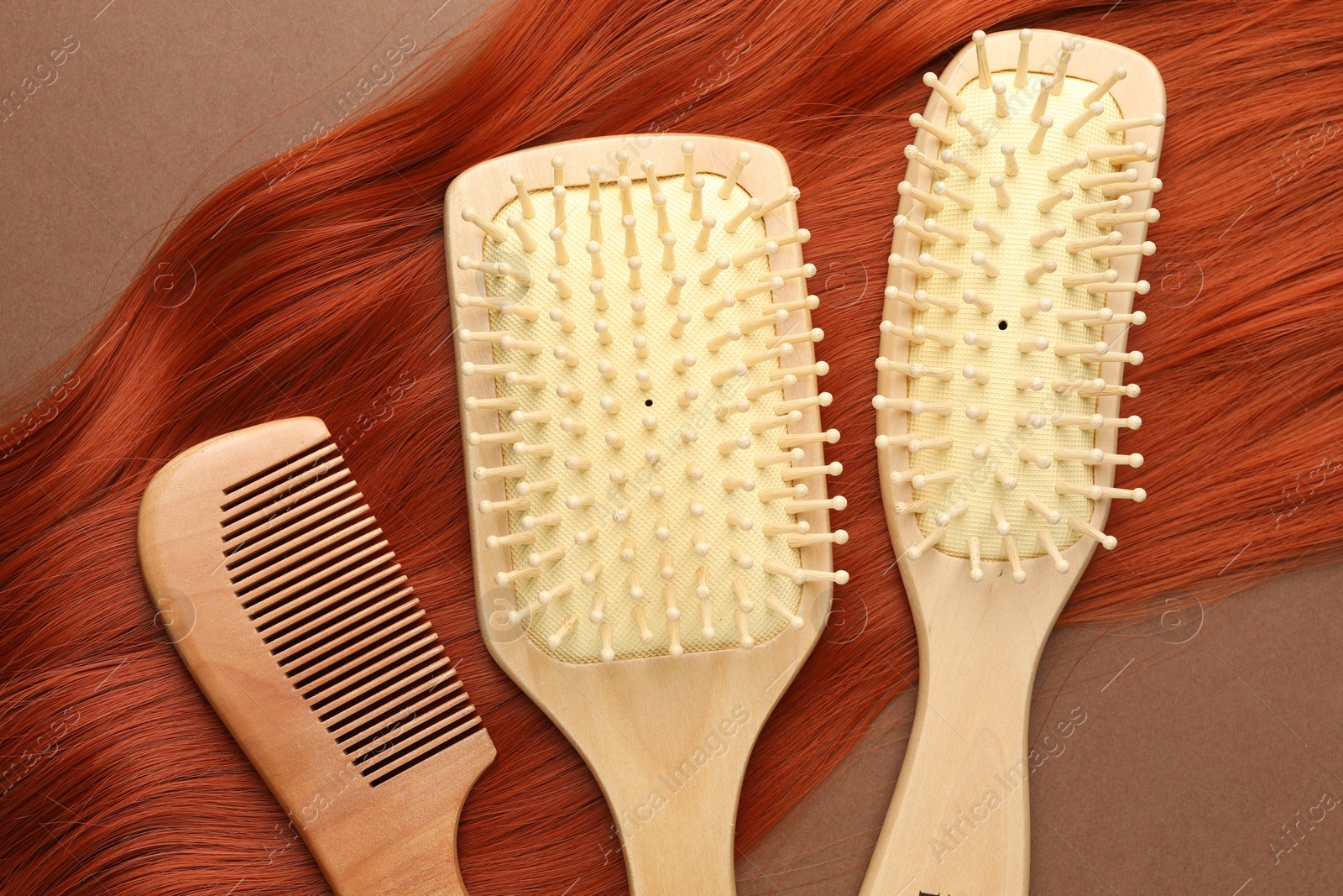 Photo of Brushes, comb and lock of hair on brown background, flat lay