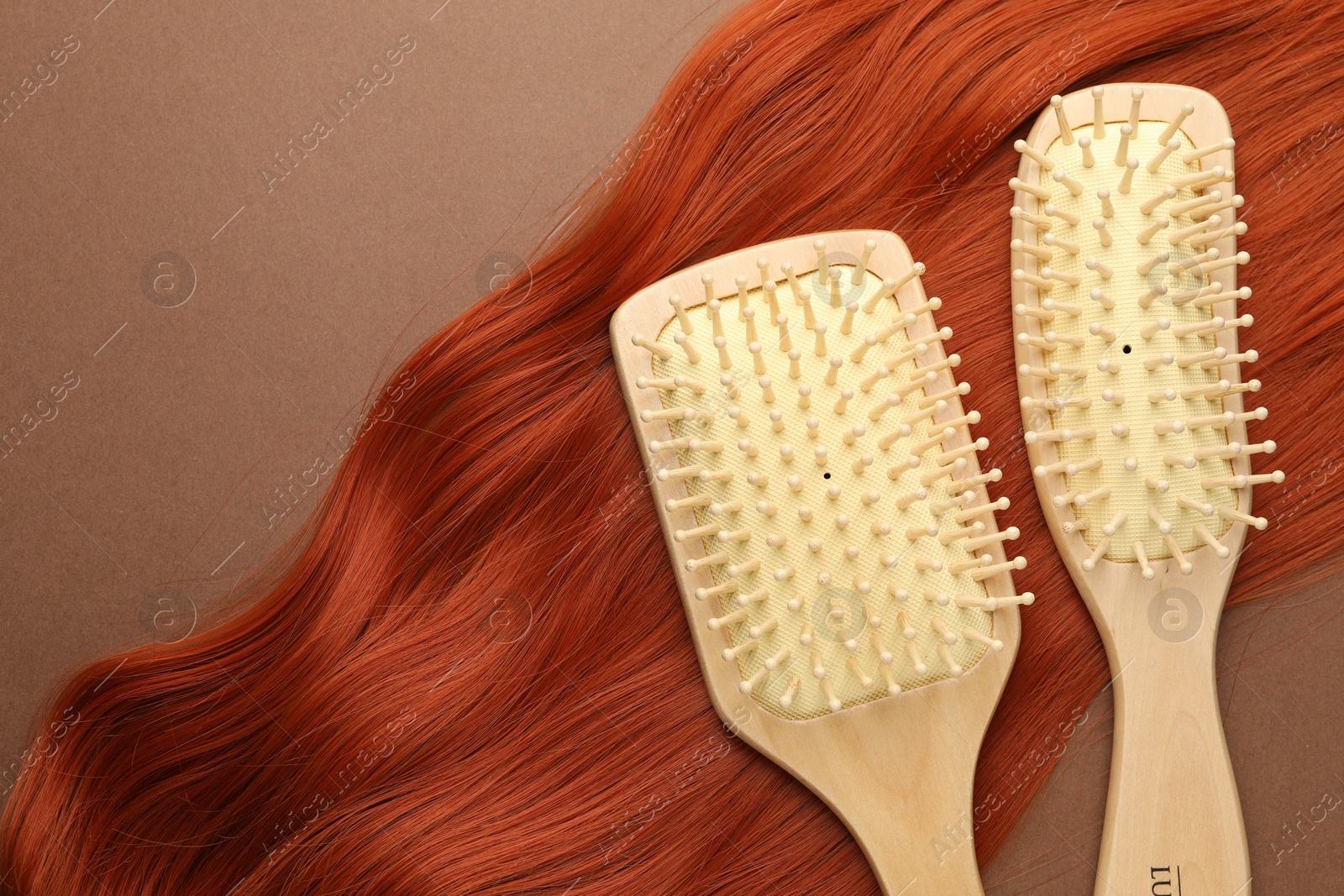 Photo of Brushes and lock of hair on brown background, flat lay