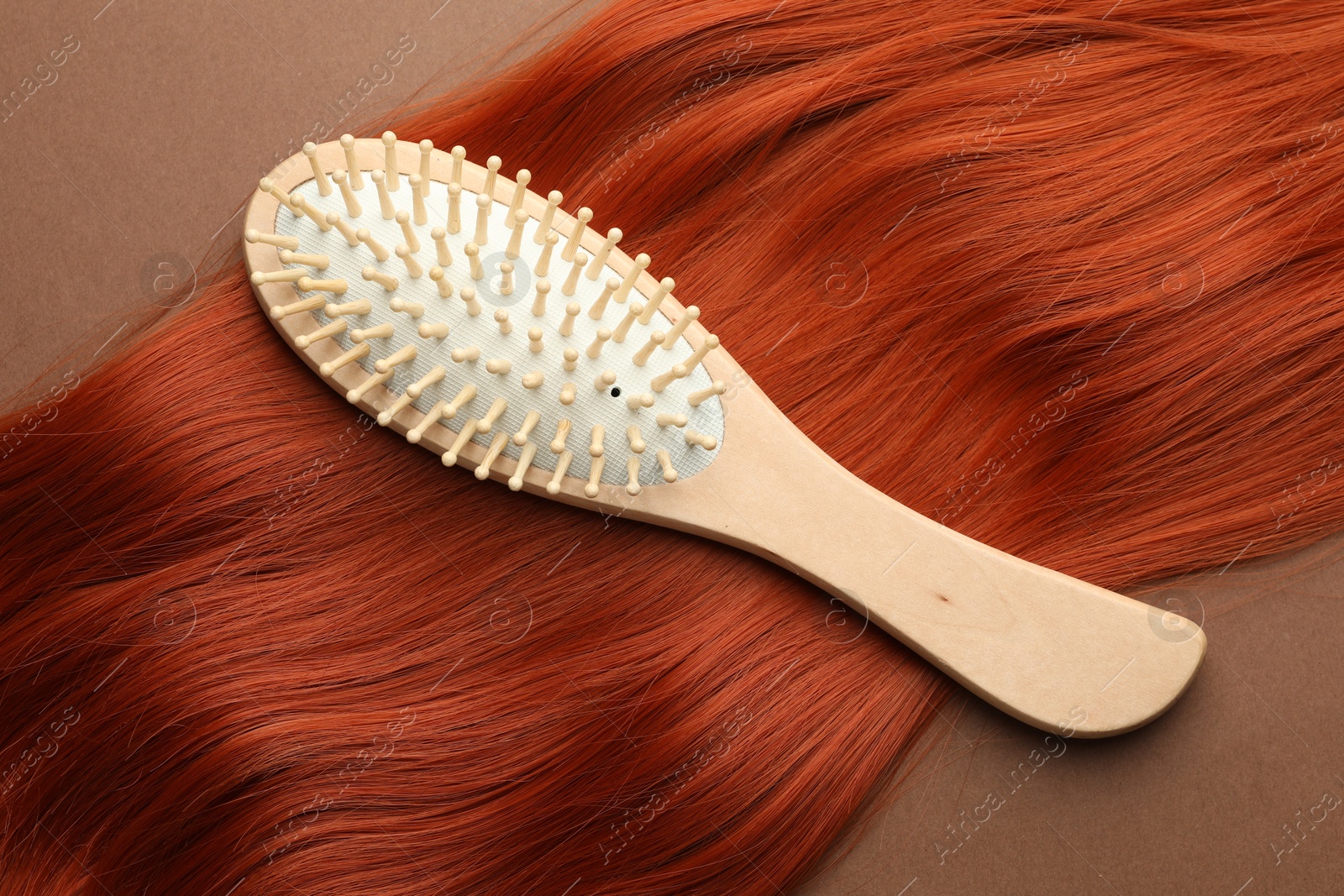 Photo of Wooden brush and lock of hair on brown background, top view