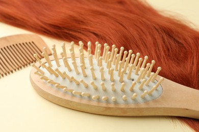 Photo of Wooden brush, comb and lock of hair on beige background, closeup