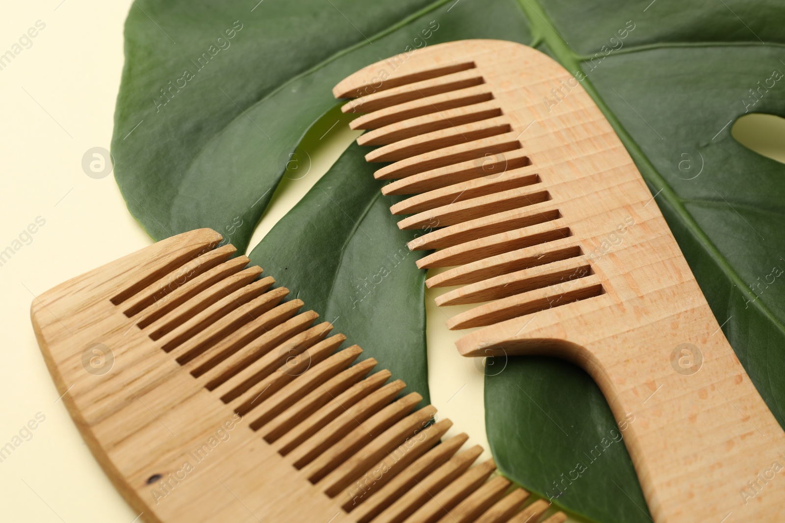 Photo of Wooden combs and monstera leaf on beige background, closeup