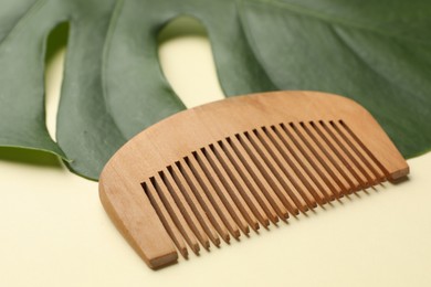 Photo of Wooden comb and monstera leaf on beige background, closeup