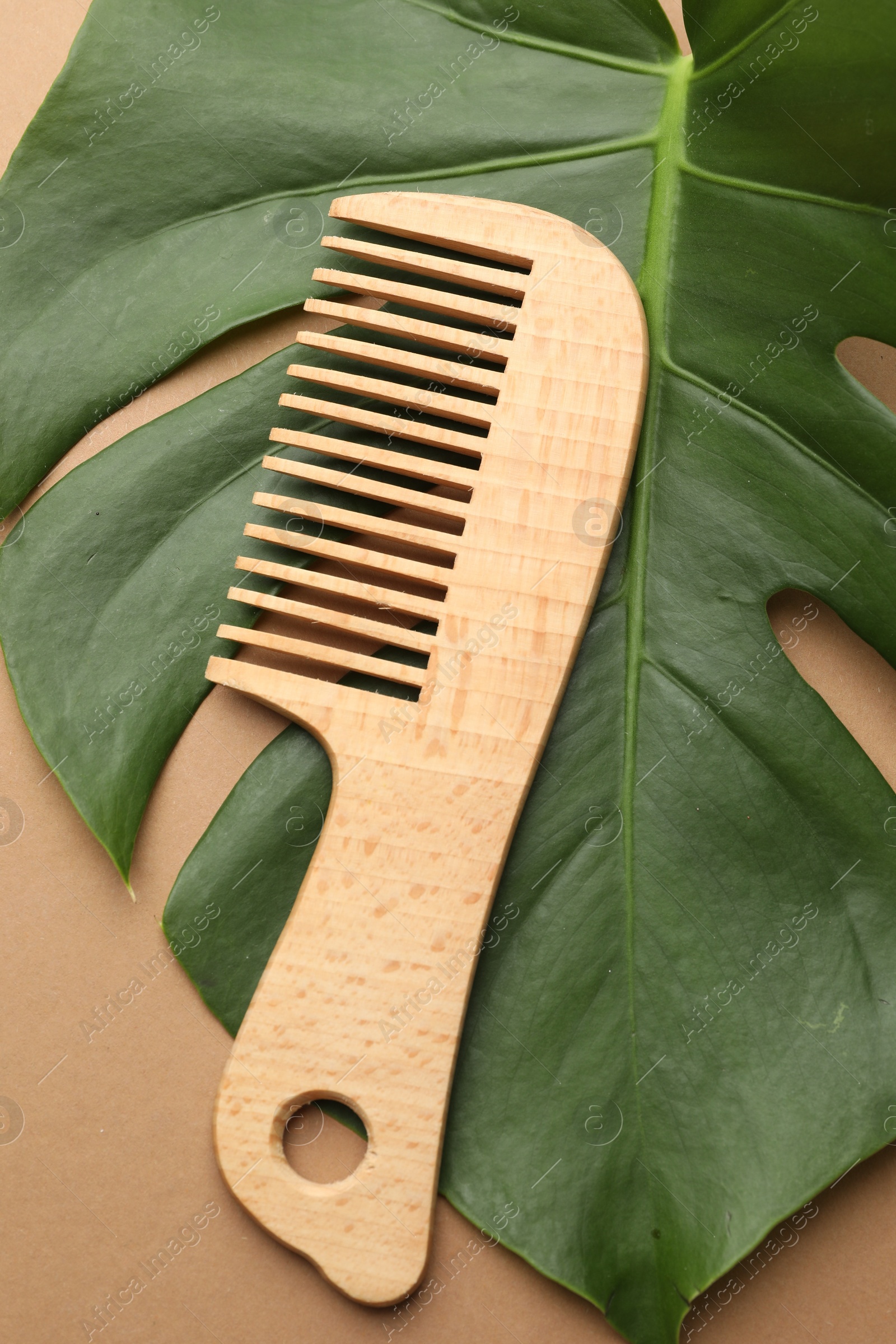 Photo of Wooden comb and monstera leaf on beige background, top view