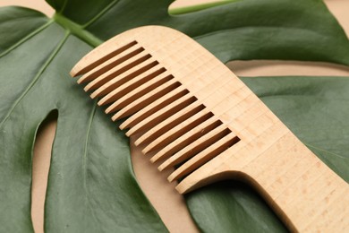 Photo of Wooden comb and monstera leaf on beige background, closeup