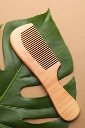 Photo of Wooden comb and monstera leaf on beige background, top view