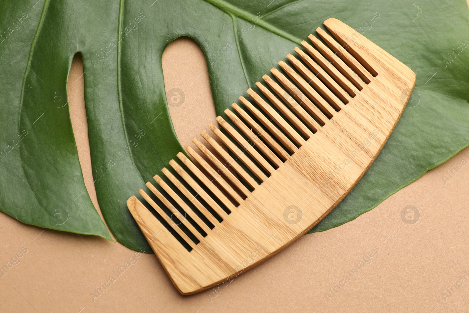 Photo of Wooden comb and monstera leaf on beige background, top view