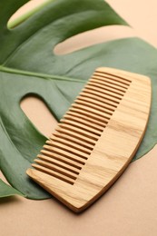 Photo of Wooden comb and monstera leaf on beige background, closeup