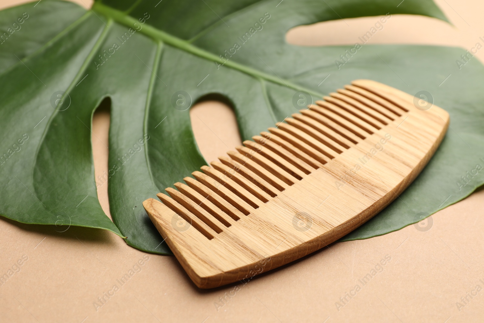 Photo of Wooden comb and monstera leaf on beige background, closeup