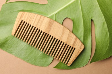 Photo of Wooden comb and monstera leaf on beige background, top view