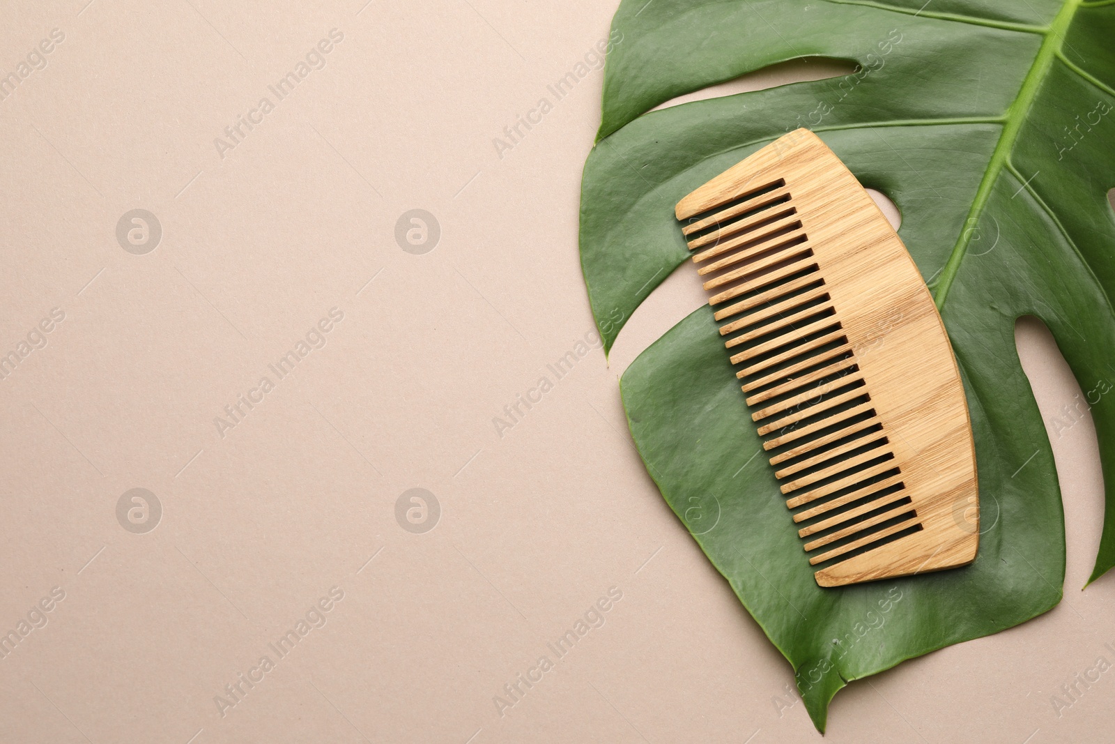 Photo of Wooden comb and monstera leaf on beige background, top view. Space for text