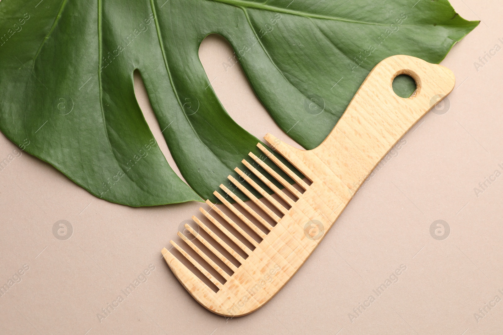 Photo of Wooden comb and monstera leaf on beige background, flat lay