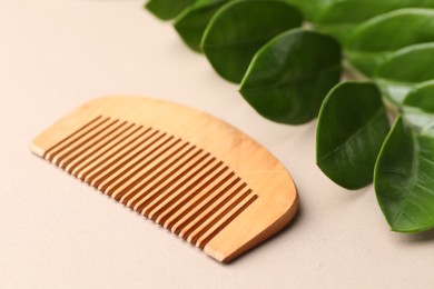 Photo of Wooden comb and branch with leaves on beige background, closeup