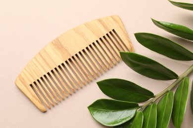 Photo of Wooden comb and branch with leaves on beige background, flat lay