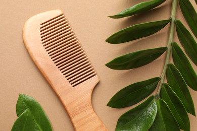 Photo of Wooden comb and branch with leaves on beige background, flat lay