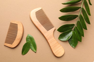 Photo of Wooden combs and branch with leaves on beige background, flat lay