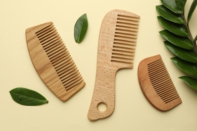 Photo of Wooden combs and branch with leaves on beige background, flat lay